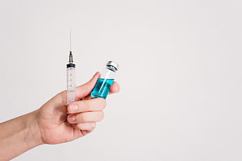 Hand holding a syringe and vaccine vial on a white background, symbolizing healthcare and immunization. HD wallpaper
