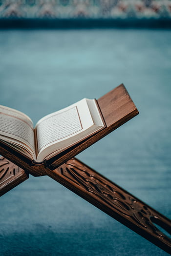 An open Quran displayed on an intricately designed wooden stand, evoking spiritual tranquility. HD phone wallpaper