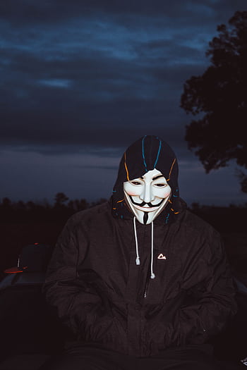 A person wearing a Guy Fawkes mask under a hooded jacket, symbolizing anonymity and mystery. HD phone wallpaper