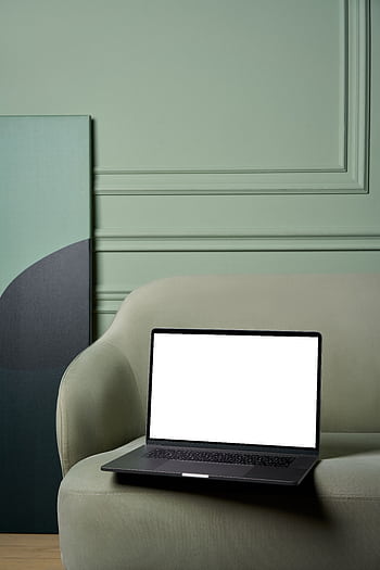 A sleek laptop with a blank screen on a stylish green sofa in a minimalist interior setting. HD phone wallpaper