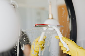 Person using a squeegee to clean a foamy bathroom mirror indoors. HD wallpaper
