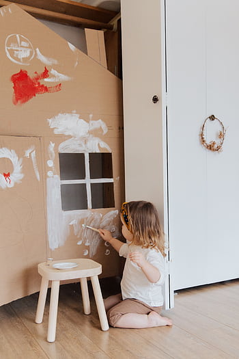 Little girl painting a cardboard house in a cozy indoor setting, expressing creativity. HD phone wallpaper