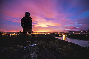 Blurry figure observing city lights at twilight on a scenic overlook, long exposure capture. HD wallpaper