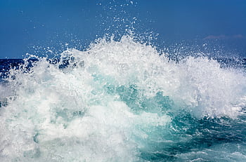 Powerful ocean waves crashing with a dramatic splash under a clear blue sky. HD wallpaper