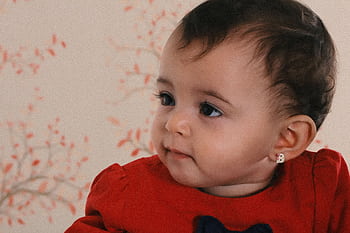 Adorable baby girl with earrings in a red dress, smiling indoors. HD wallpaper