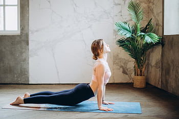 Woman in yoga pose on mat, exercising indoors with natural light and plant decor. HD wallpaper