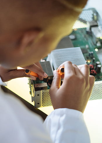 Close-up of a technician repairing a circuit board with precision in a workshop. HD phone wallpaper