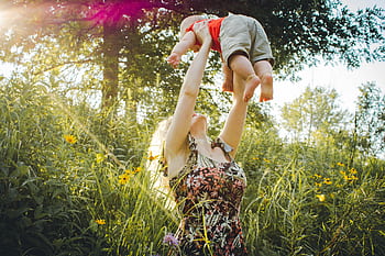 A joyful mother lifts her baby in a sunny summer meadow, capturing a moment of love and happiness. HD wallpaper