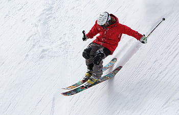 A skier in a red jacket descends a steep snowy slope, showcasing skill and adventure in winter sports. HD wallpaper
