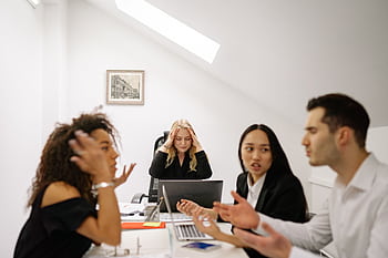 Colleagues in a heated discussion around a desk, highlighting workplace stress and tension. HD wallpaper