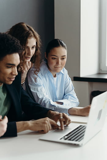 A diverse team of professionals collaborating on a laptop in an office setting. HD phone wallpaper
