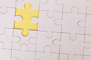 Close-up of a white jigsaw puzzle with a single yellow piece missing, symbolizing incompleteness. HD wallpaper