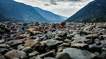 Rocky riverbank in Little Fort, BC offers a serene view of mountains and water. HD wallpaper