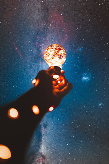 A hand holds a glowing bulb into the Milky Way night sky, creating a magical cosmic connection. HD phone wallpaper