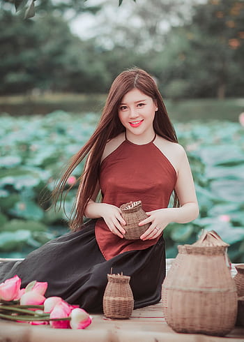 An Asian woman sits with baskets among lotus flowers, exuding elegance and serenity. HD phone wallpaper