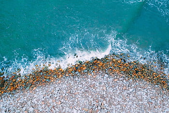 A stunning aerial view capturing the contrast between rocky shores and azure ocean waves. HD wallpaper