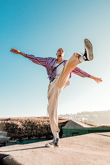 Man in stylish outfit poses dynamically on a rooftop under clear blue skies. HD phone wallpaper
