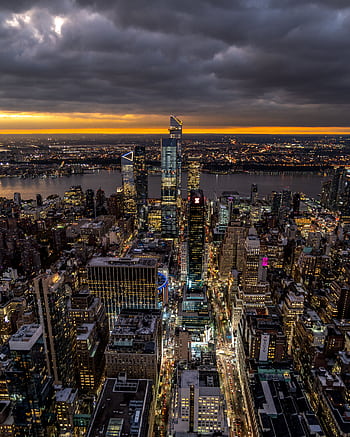 Aerial view of New York City's vibrant skyline during dusk with dramatic clouds and city lights. HD phone wallpaper