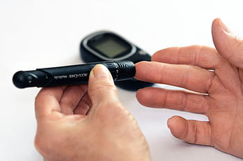 Close-up of a person using a glucometer for diabetes management indoors. HD wallpaper