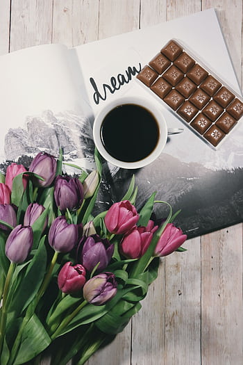 A warm setup featuring a cup of black coffee, colorful tulips, and chocolate on a wooden table. HD phone wallpaper
