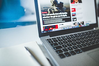Open laptop displaying an online news article on a desk with a notebook nearby. HD wallpaper