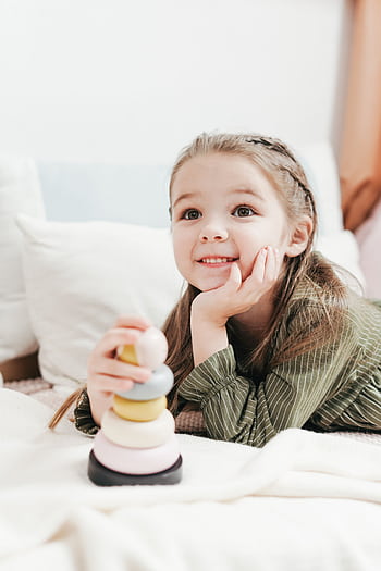Adorable child playing happily with a stacking toy on the bed indoors. HD phone wallpaper