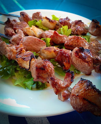 Delicious grilled meat skewers on a bed of fresh greens, perfect for a barbecue meal. HD phone wallpaper