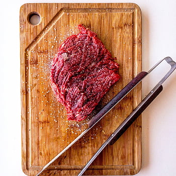 Top view of seasoned raw beef steak on wooden board with tongs, ready for cooking. HD phone wallpaper