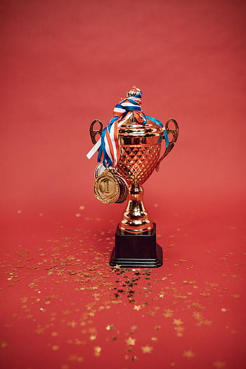Golden trophy adorned with medals on a red backdrop surrounded by scattered confetti. HD phone wallpaper
