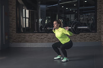 Dedicated woman in neon activewear performs a weighted squat in an indoor gym setting. HD wallpaper