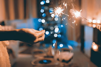 Hands holding sparklers in a festive indoor setting with blurred lights and bokeh effect. HD wallpaper