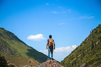 A solo backpacker standing on a rock, admiring the mountain view under a bright blue sky. HD wallpaper
