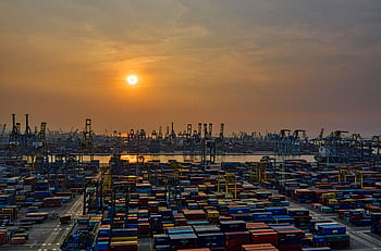 Sunset over a bustling seaport filled with stacked shipping containers and cranes. HD wallpaper