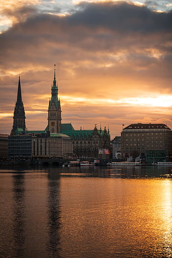 Dramatic view of Hamburg's skyline at sunset featuring iconic architecture and vivid water reflections. HD phone wallpaper