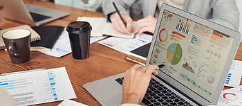 Professionals engaged in a business meeting, analyzing data and charts on laptops and papers. HD wallpaper