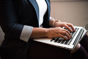 Woman in a blazer typing on a laptop in a well-lit room, focused on remote work. HD wallpaper
