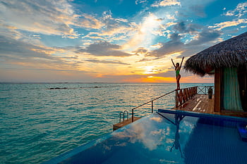 Woman enjoying a stunning sunset at a luxury Maldives resort's infinity pool. HD wallpaper