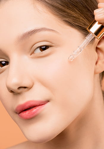 A woman applying serum with a dropper to her face for skincare routine. HD phone wallpaper