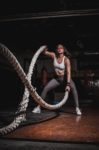 Female athlete demonstrating strength with battle ropes in a gym. HD phone wallpaper