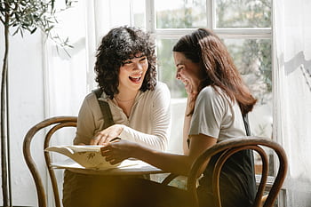 Joyful conversation between two women enjoying time together indoors. HD wallpaper