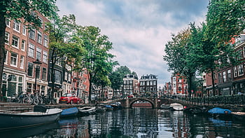 Charming view of an Amsterdam canal lined with bicycles, boats, and historic buildings. HD wallpaper