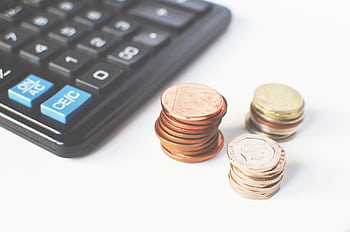 Close-up of stacked coins and a calculator symbolizing financial strategy and budgeting. HD wallpaper