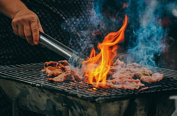 Close-up of grilling meat with vibrant flames and smoky aura, showcasing outdoor cooking. HD wallpaper