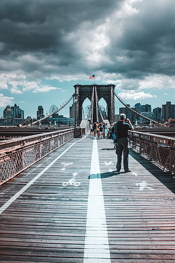 Iconic view of Brooklyn Bridge filled with pedestrians under dramatic skies. HD phone wallpaper