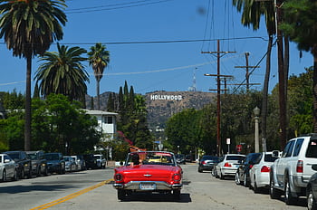 Red convertible driving down a sunny street towards the iconic Hollywood sign in Los Angeles. HD wallpaper