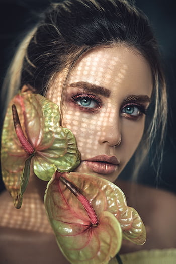 Close-up portrait of a woman with vibrant makeup and anthurium flowers, featuring dramatic lighting. HD phone wallpaper