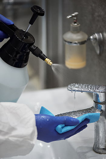 A person wearing gloves sprays and wipes a bathroom faucet for hygiene. HD phone wallpaper