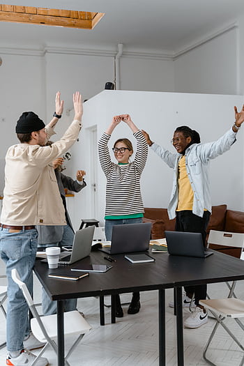 A multicultural group of professionals celebrating success in a modern office setting, emphasizing teamwork and collaboration. HD phone wallpaper