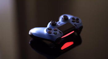 Close-up of a blue PlayStation controller on a glossy black surface with red lighting. HD wallpaper