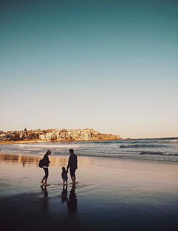 A family enjoying a peaceful walk along Bondi Beach during sunset, with city views in the background. HD phone wallpaper